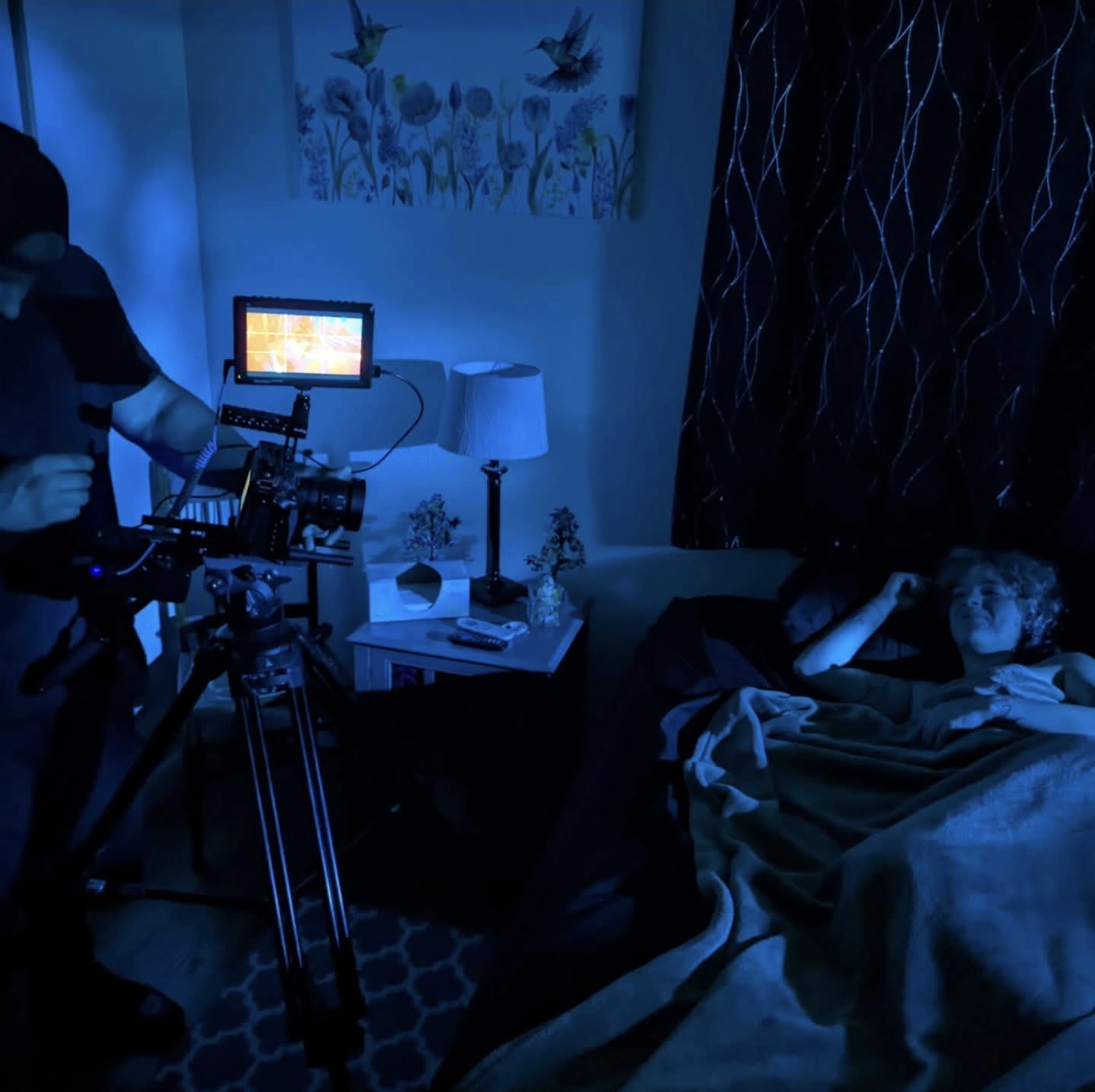 Camera and monitor set up to film a bedroom scene under blue lighting.